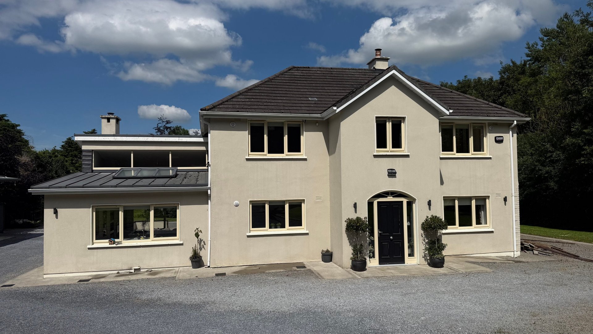 Modern two-story cream-colored residential house with black roof, large windows, and contemporary architecture
