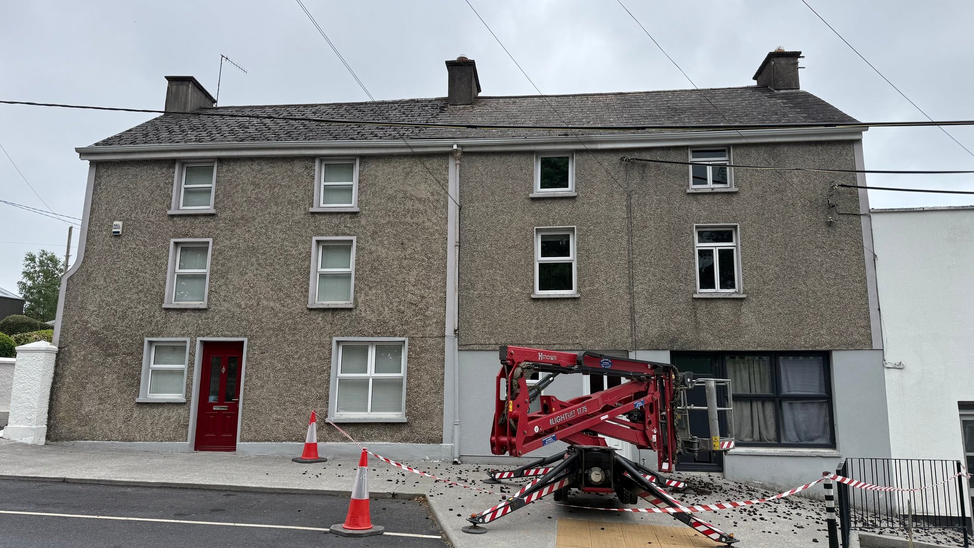 Stone building under renovation with red construction lift, traffic cones, and barriers in front