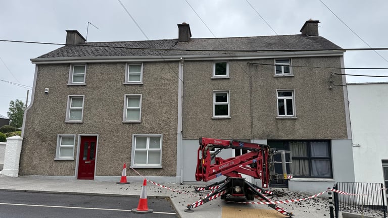 Stone building under renovation with red construction lift, traffic cones, and barriers in front