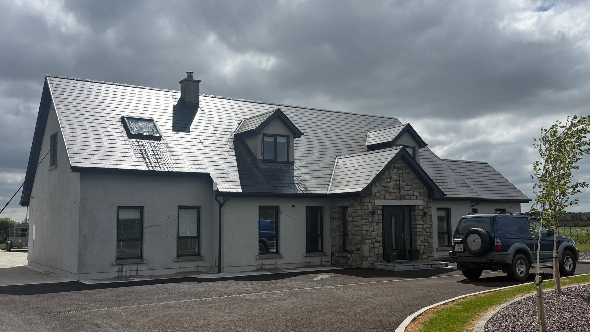 Modern residential house with mixed stone and white render exterior, pitched roof, and parked vehicle on driveway